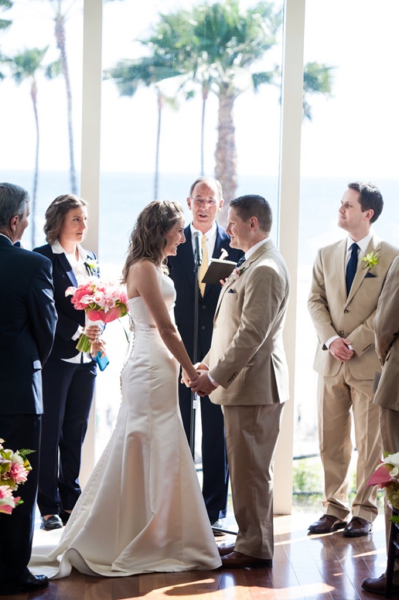Wedding ceremony with Kyle and Kate holding hands before Uncle Darryl, ocean and palm trees through the window