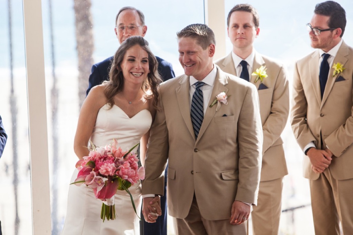 Bride and groom smiling and holding hands at the altar with pink bouquet