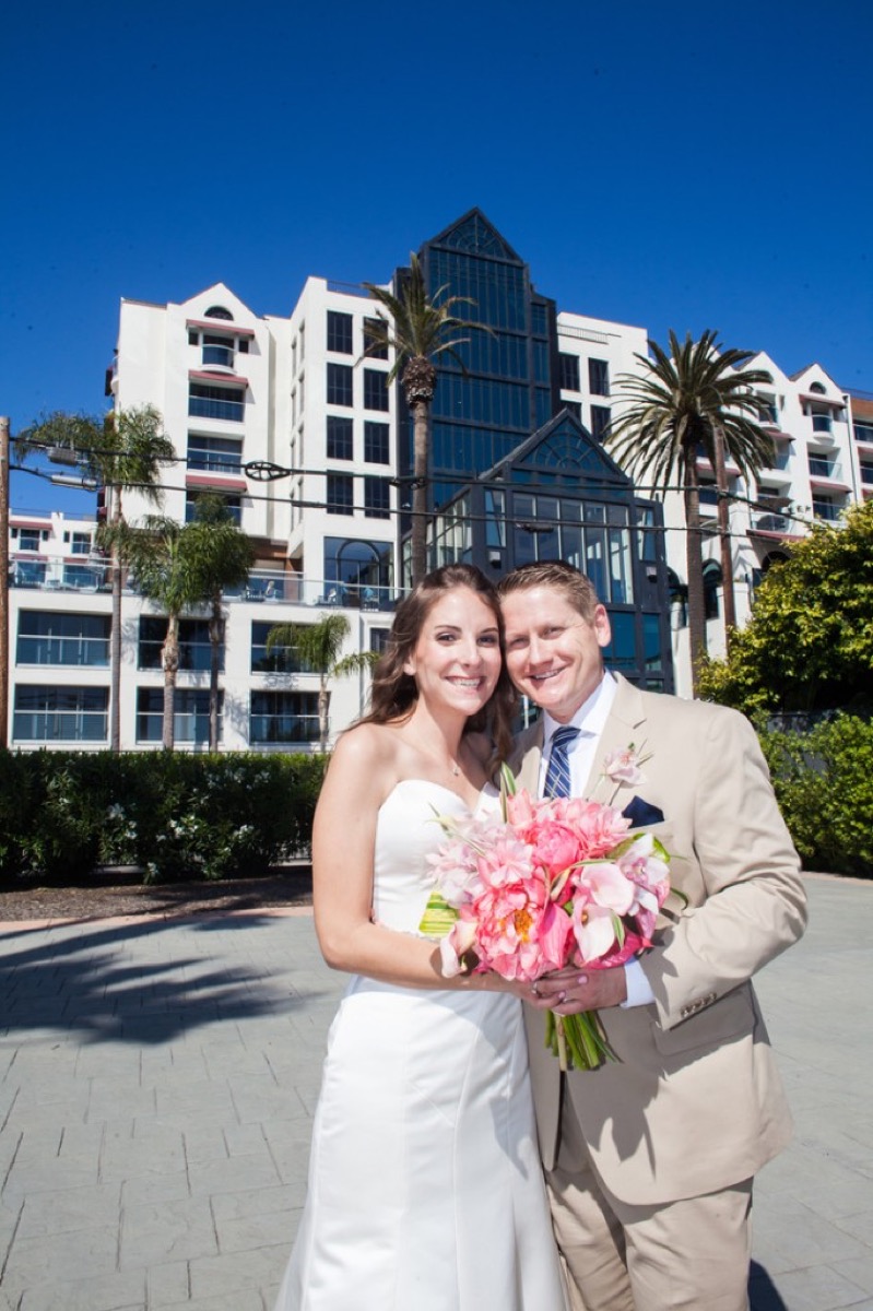 Kyle and Kate in tan suit and white gown holding a pink bouquet outdoors at Loews Santa Monica