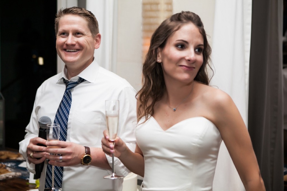 Kyle speaking into a microphone with Kate holding champagne