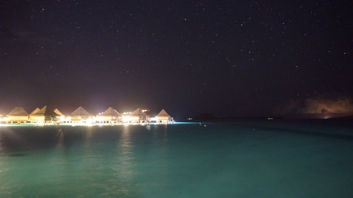 Overwater bungalows at night with glowing turquoise water and stars