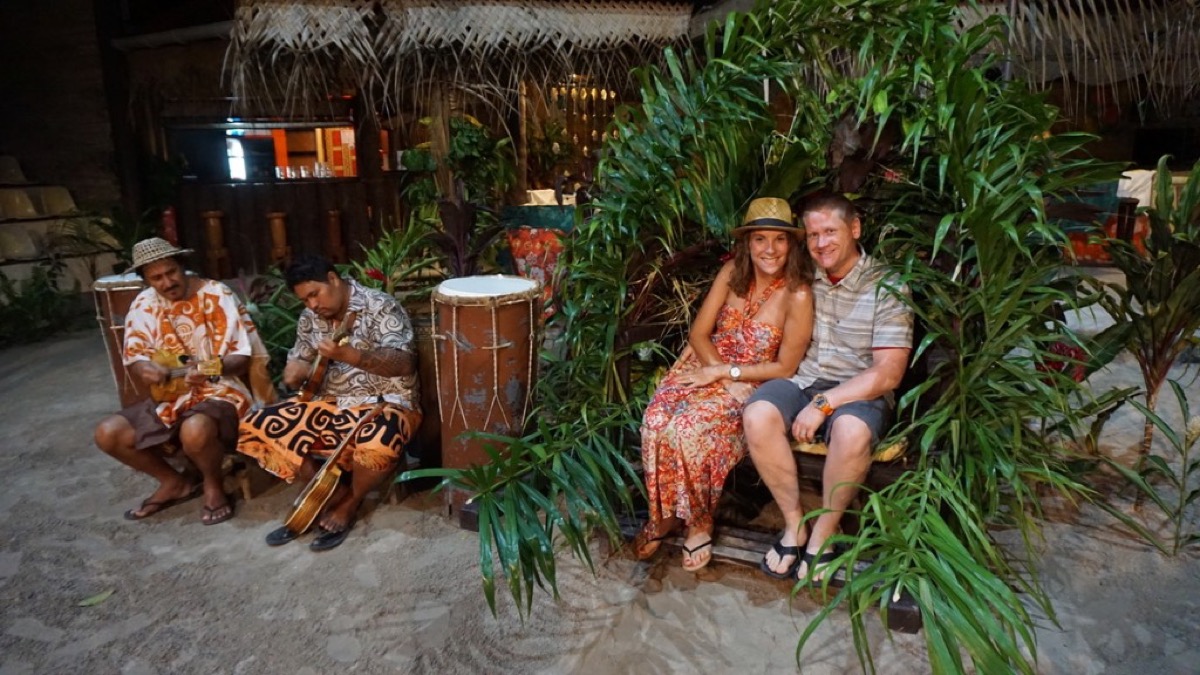 Kyle and Kate on a palm-frond bench with musicians at a Moorea luau