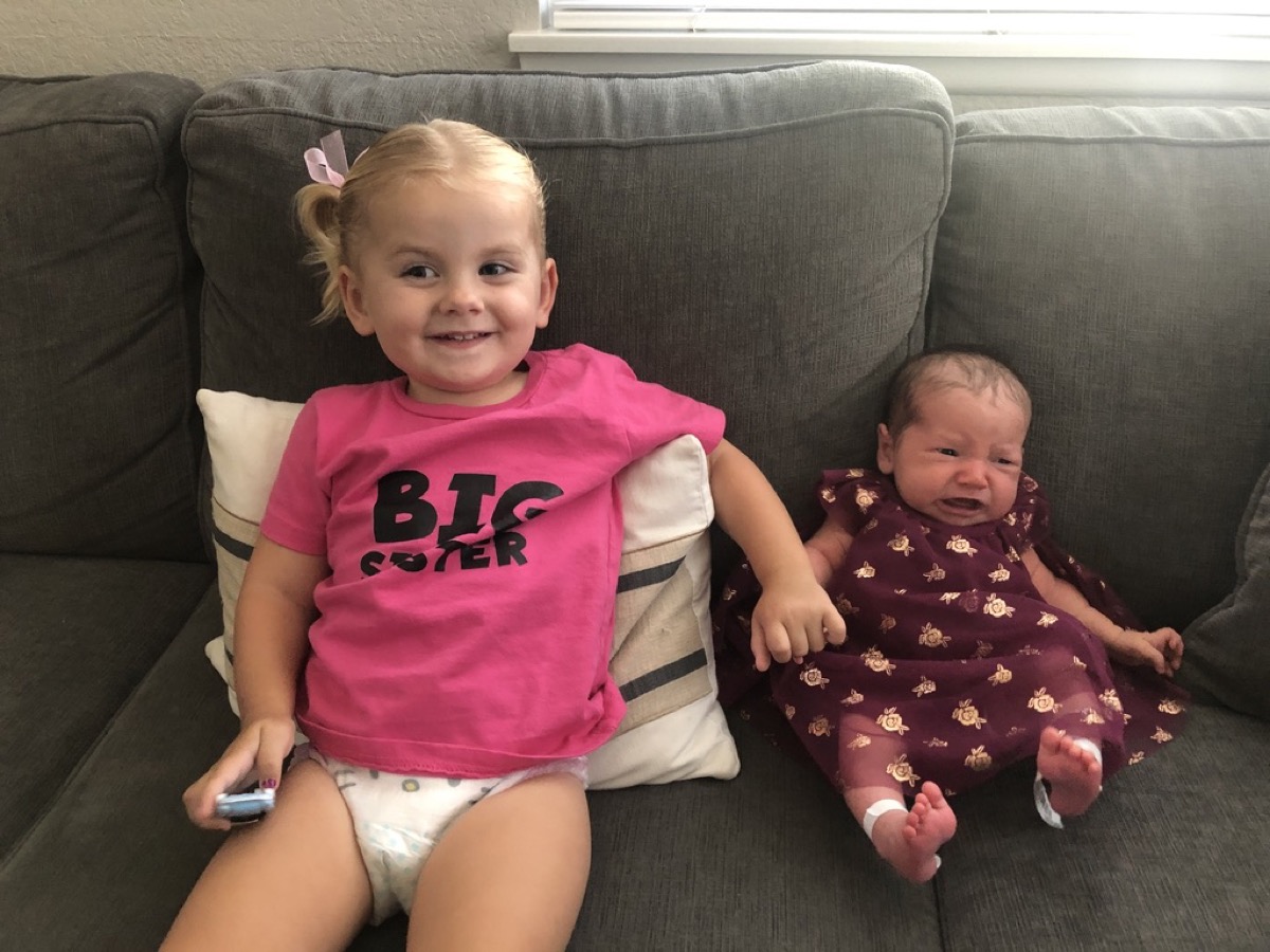 Makena in a BIG SISTER shirt sitting with newborn Morgan on the couch