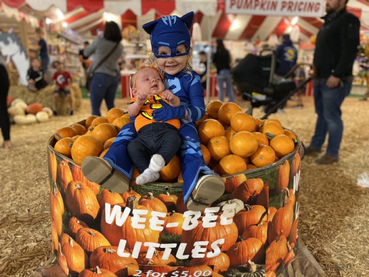 Makena in a Catboy costume holding baby Morgan in a pumpkin patch bin