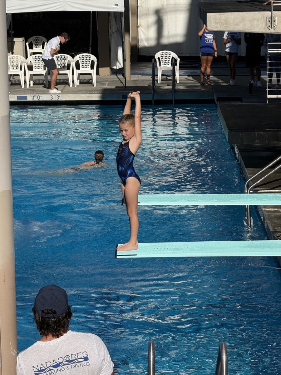 Makena in a competitive dive reach position on a diving board at the pool