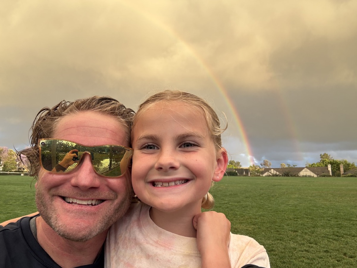 Kyle and Makena selfie on a soccer field with a double rainbow behind storm clouds