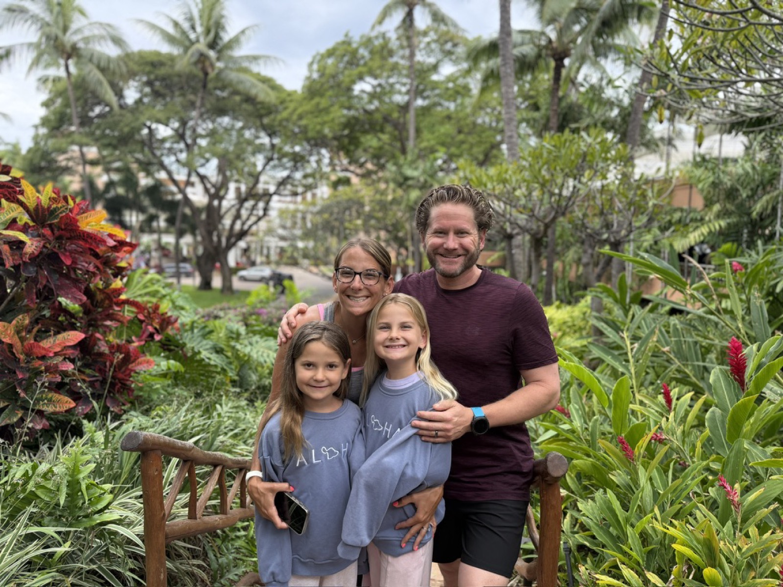Kyle, Kate, Makena, and Morgan in a lush Maui garden on a wooden bridge, wearing matching ALOHA sweatshirts