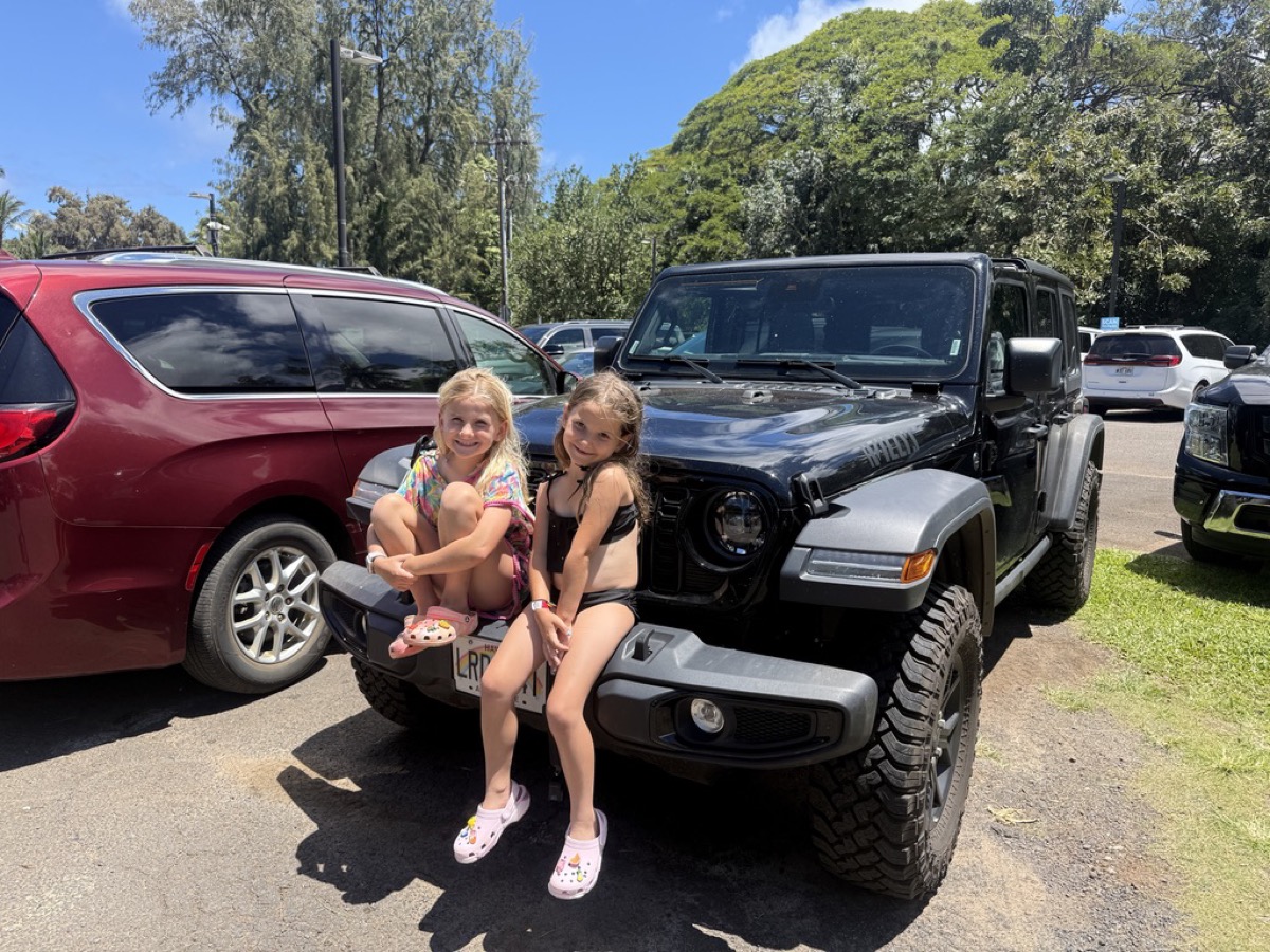 Makena and Morgan sitting on the front of the family Jeep in Maui